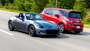 a woman driving a convertible car next to a red car