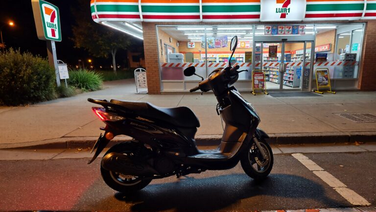 Scooter estacionado afuera de un 7-Eleven de noche.